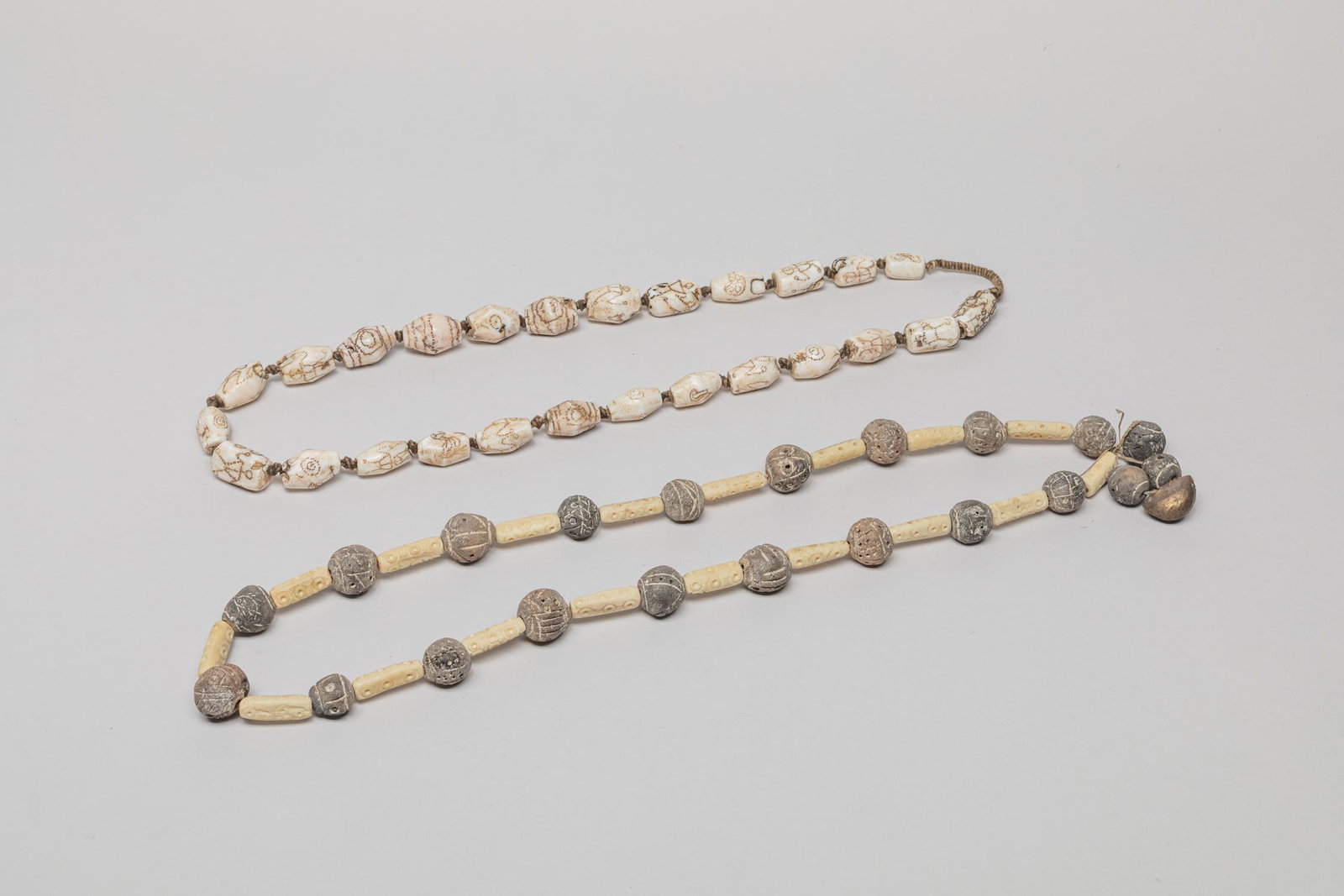 Naga Clay, Bone & Stone Large Bead Necklace: Including a Naga type large clay and bone bead necklace suspended with a bell and a large stone bead necklace carved with abstract pattern. 28inch L (larger).