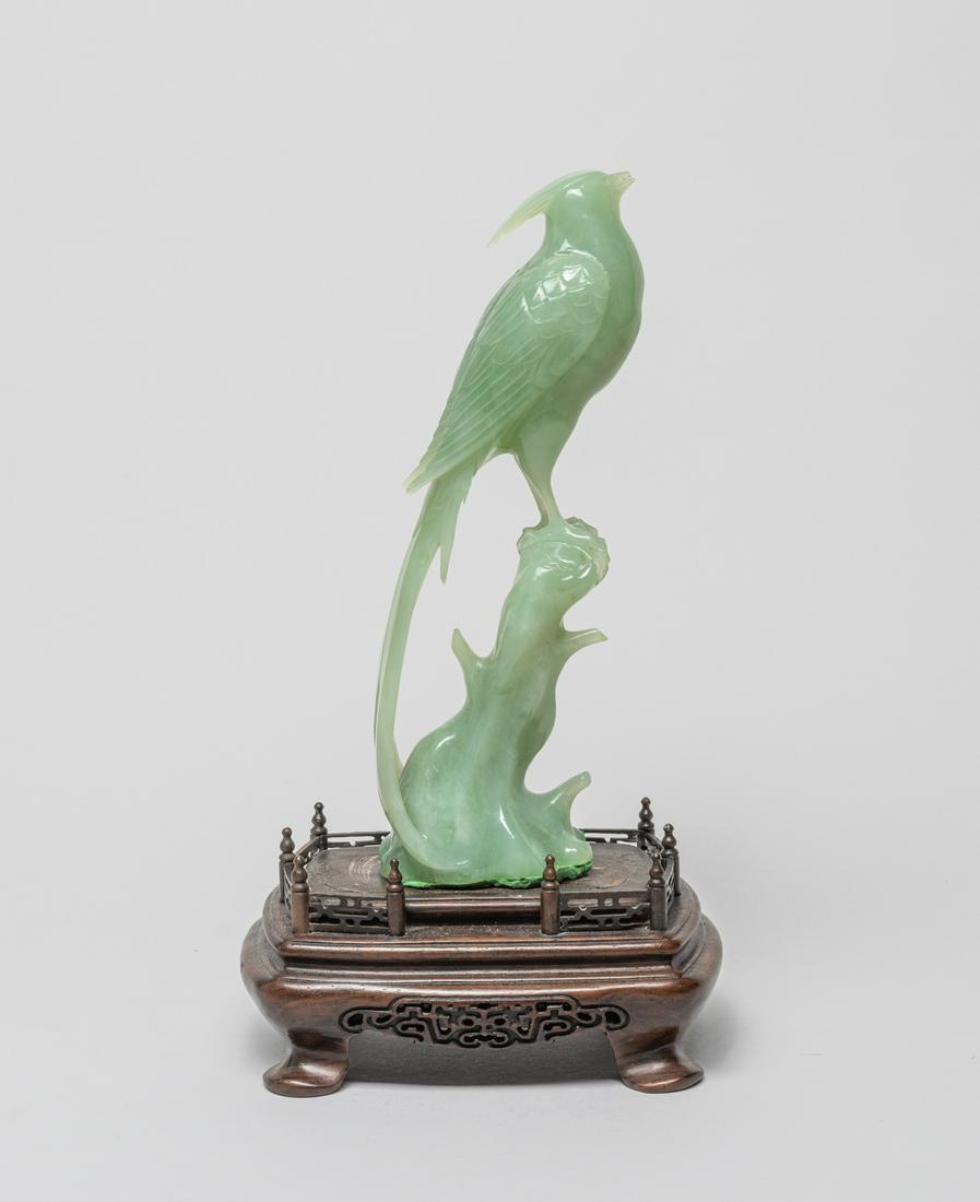 Chinese Translucent Jade Bird With Stand: Carved in the form of a bird standing on a gnarled branch, the stone in a translucent celadon color, with a wood stand. 10.3inch H, 5.7inch L, 3.8inch W.