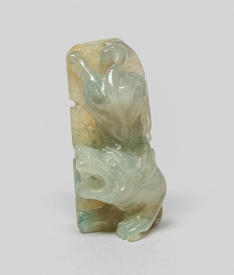 Chinese Clear Jade Jadeite Toggle: Deftly carved as a beast with ferocious expression above a pine tree issuing rockwork, its head turned sharply to the right, the stone in pale celadon tone with faint russet inclusions. 1.85inch L, 0.