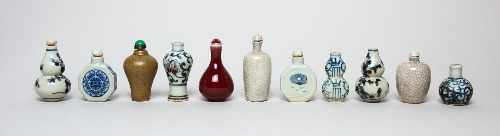 Collectible Chinese Porcelain Snuff Bottles: Group of 11 porcelain snuff bottles in double-gourd, ovoid, flattened, or vase form, five decorated with foliages, one with bats and shou characters, one with a figure, the other four applied with red