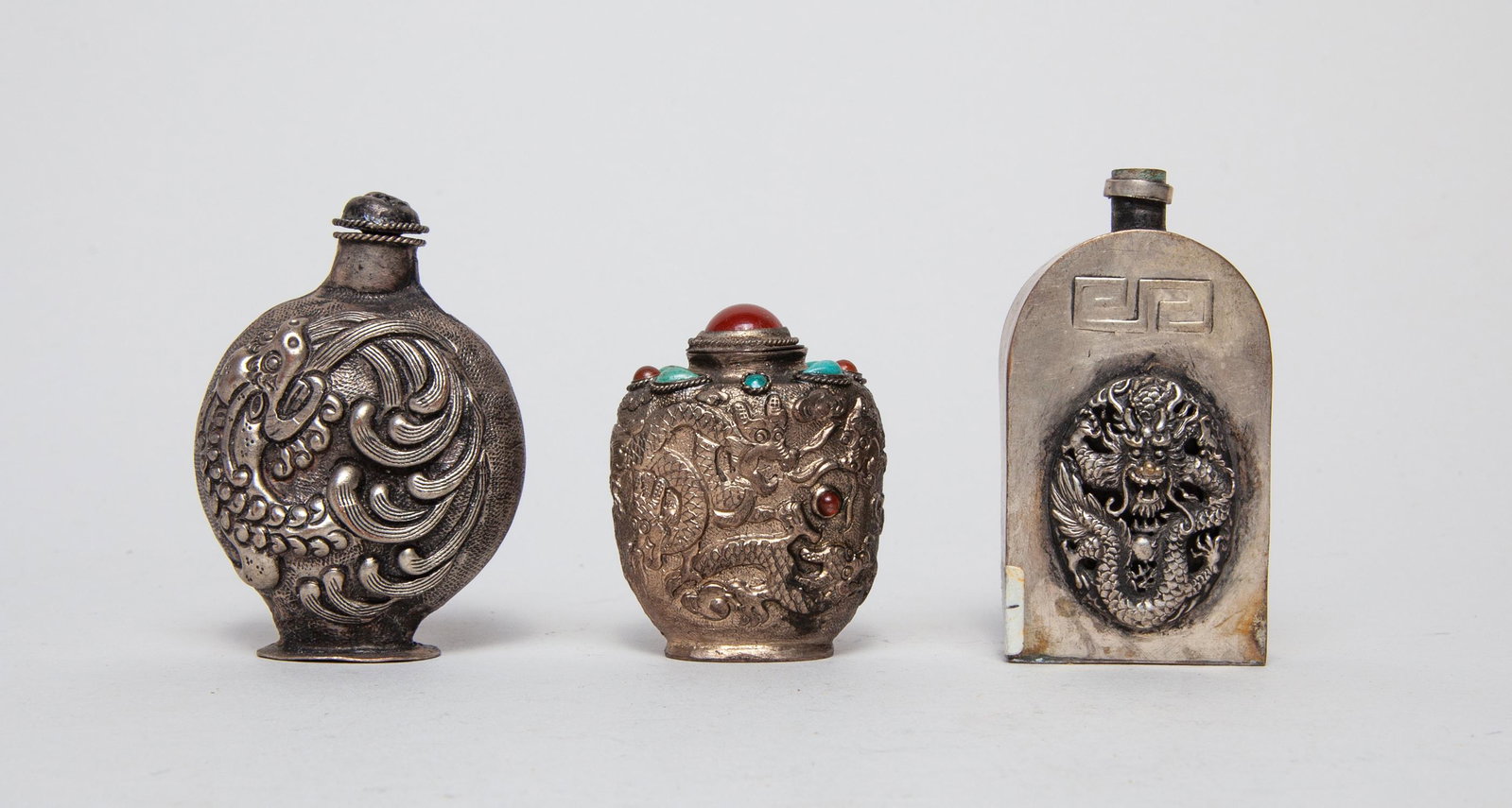 Set Chinese Silver Color Snuff Bottle: Three as a group, one of rounded form cast with a raised beast to either side, one of spade form cast with dragons pursuing inlaid gemstone, the other of arched rectangular form cast with a raised dra