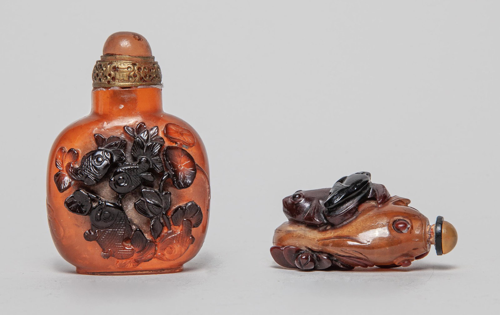 Two Chinese Amber Like Snuff Bottles: One of bulbous square form, carved in high relief with carps and lotus on one side, the reverse with goldfish and catfish, inscribed with related passages, the other snuff bottle carved in fish form, 