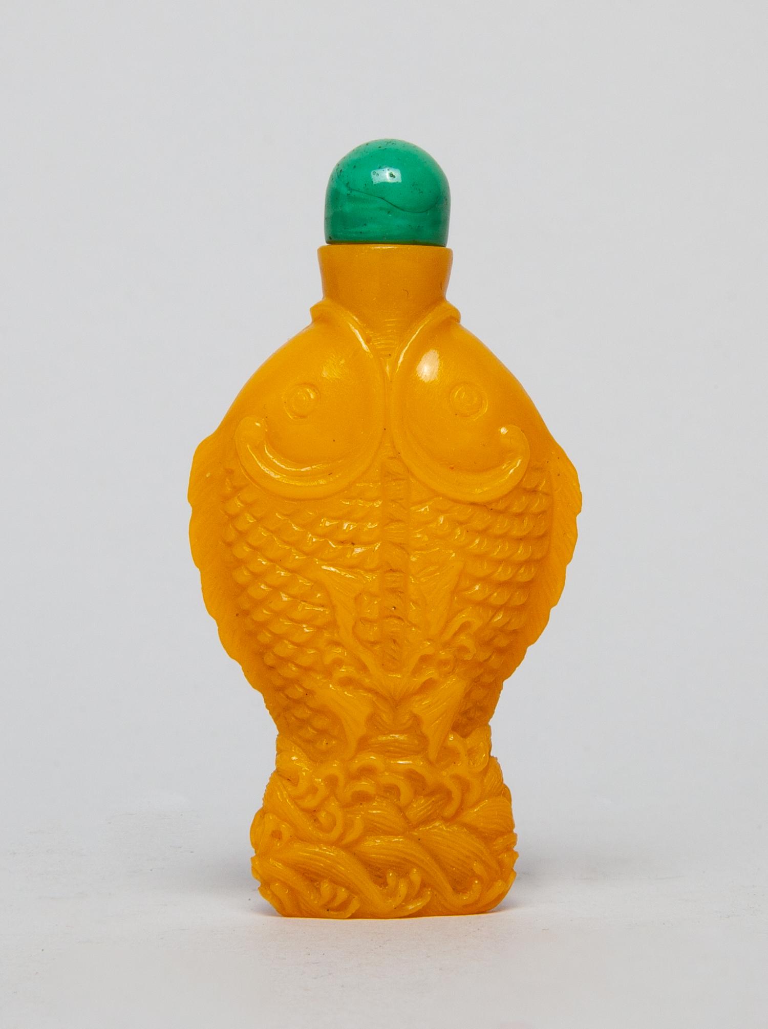 Chinese Royal Yellow Glass Snuff Bottle: Of special fish form, carved to both sides with a pair of confronting fish above waves, the glass in an opaque royal yellow tone, with a green gemstone stopper. 3.2inch L, 1.6inch W.