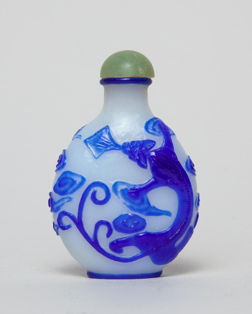 Chinese Overlay Glass Snuff Bottle: Of rounded form, with design of a recumbent beast amid clouds on either side, in blue on a milky-glass ground, with a stopper. 2.93inch H, 1.95inch W.