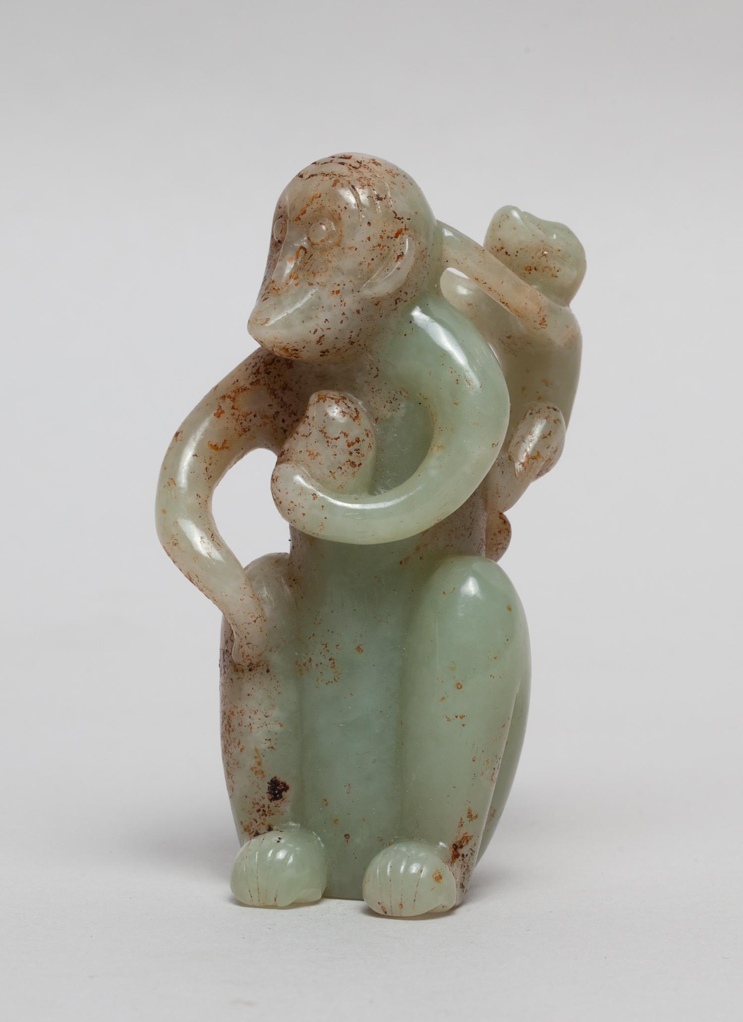 Large Chinese Russet Jade Monkey: Carved and pierced as a crouching monkey with left hand holding a peach, a young monkey clambering on its back, the stone in pale celadon tone with russet inclusions. 3.5inch H, 1.6inch W.