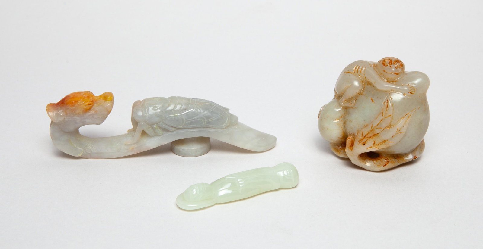 Collectible Chinese Jade Carvings: Including a russet jade carving worked in the form of a monkey clambering on a large peach borne on a gnarled branch issuing leaves and a smaller peach, a white jade carved standing Buddha, and a whit