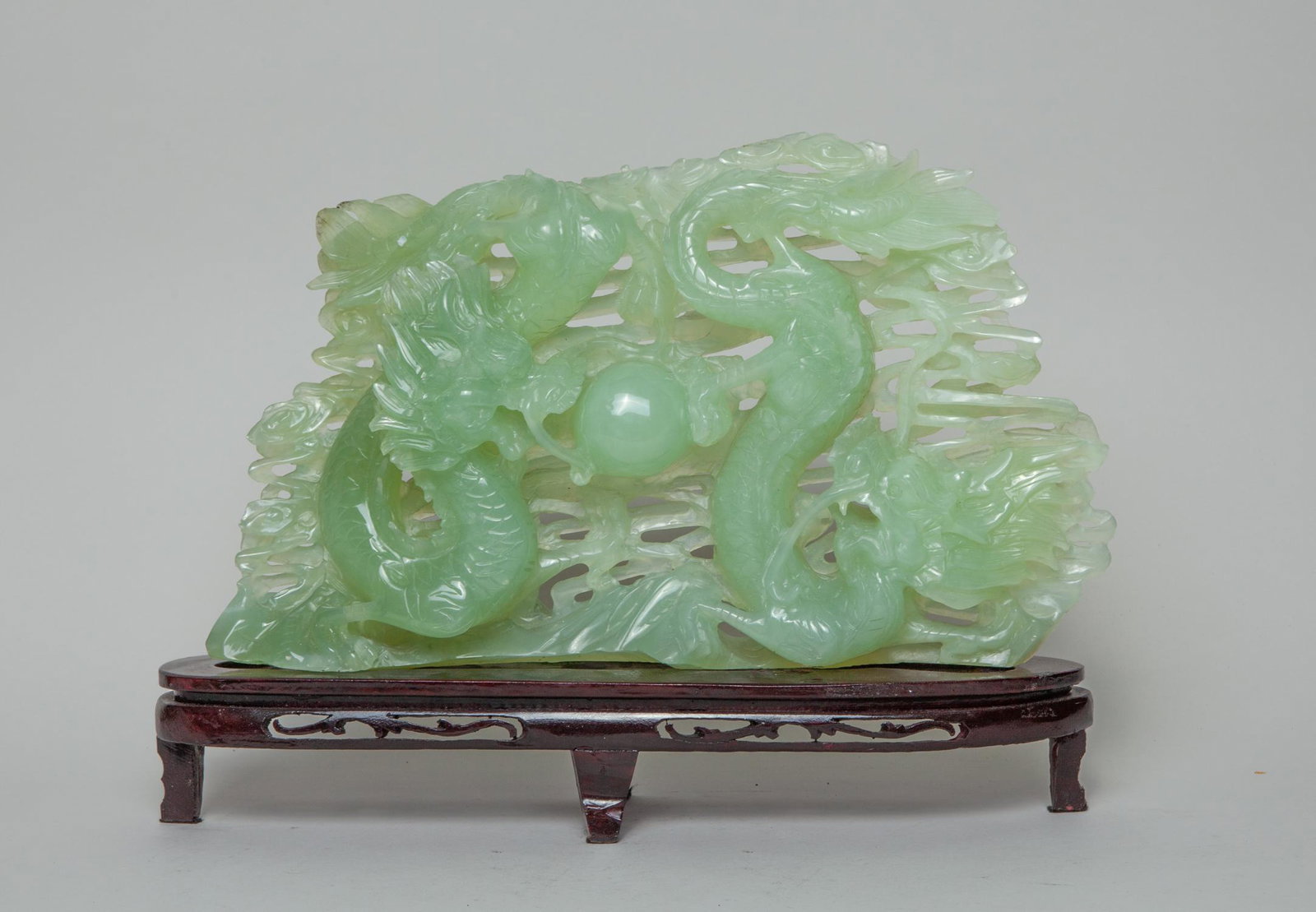Chinese Export Translucent Jade Dragon: The translucent jade skillfully carved in openwork with a pair of sinuous dragons pursuing a flaming pearl among scrolling clouds, with a wood stand and a box. Approx. 8.5inch H, 15inch W (jade only).