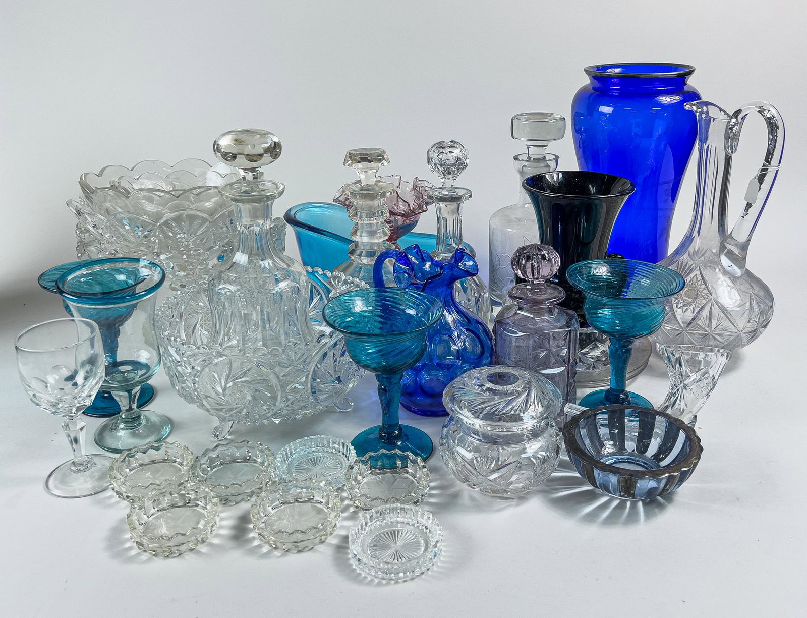 Large Group Cut Art Crystal Glass Wares: A large group of art crystal glass vases, pitchers, decanters, bowls, cups and ashtrays, the glass is clear or in varying shades of blue. 13inch H, 6.5inch D (largest).