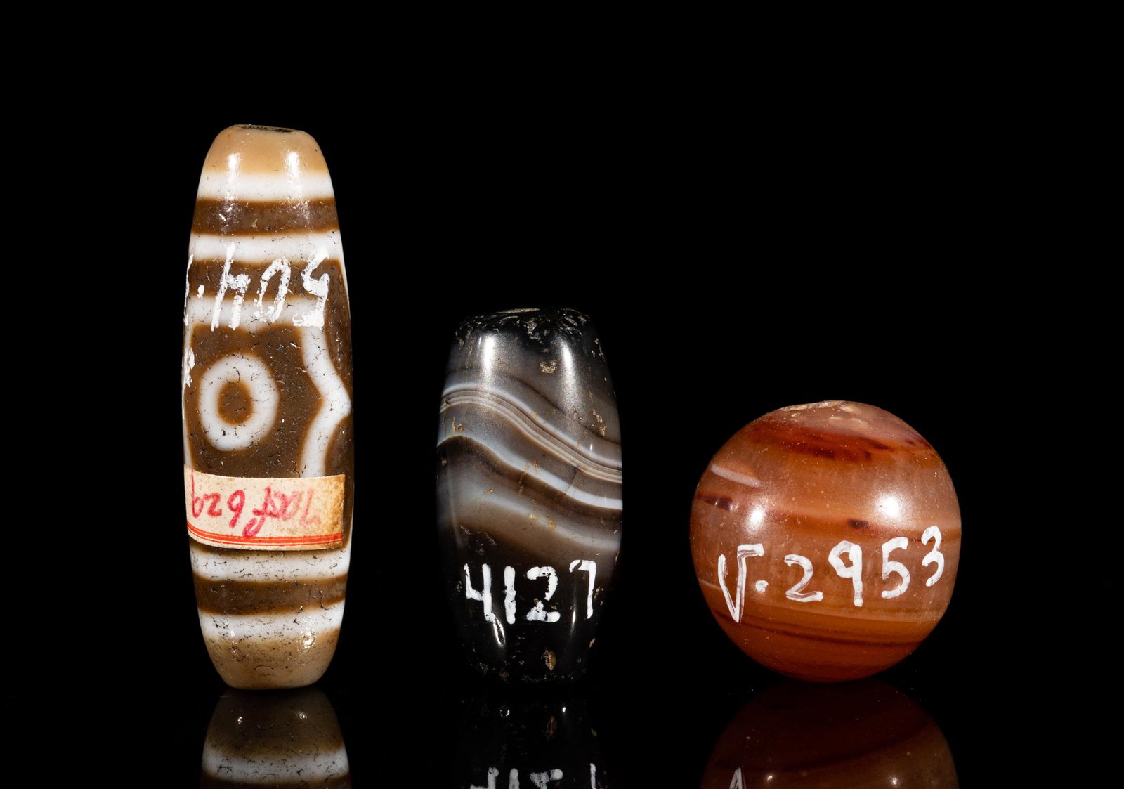 Chinese Sino-Tibetan Agate & Dzi Beads: Including two Sino-Tibetan style agate beads in sphere or ovoid form and a dzi bead. 1.5inch L, 0.45inch W (largest).
