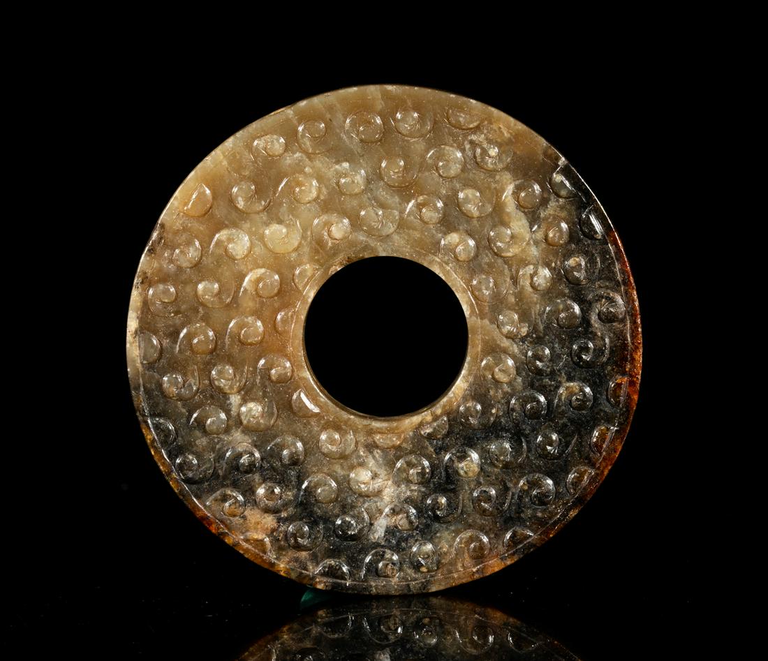 Large Chinese Jade Carved Bi: Of circular shape, carved with raised archaic spirals on both sides, the center pierced with an aperture, the stone in a variegated brown and black tone. 3.2inch D.