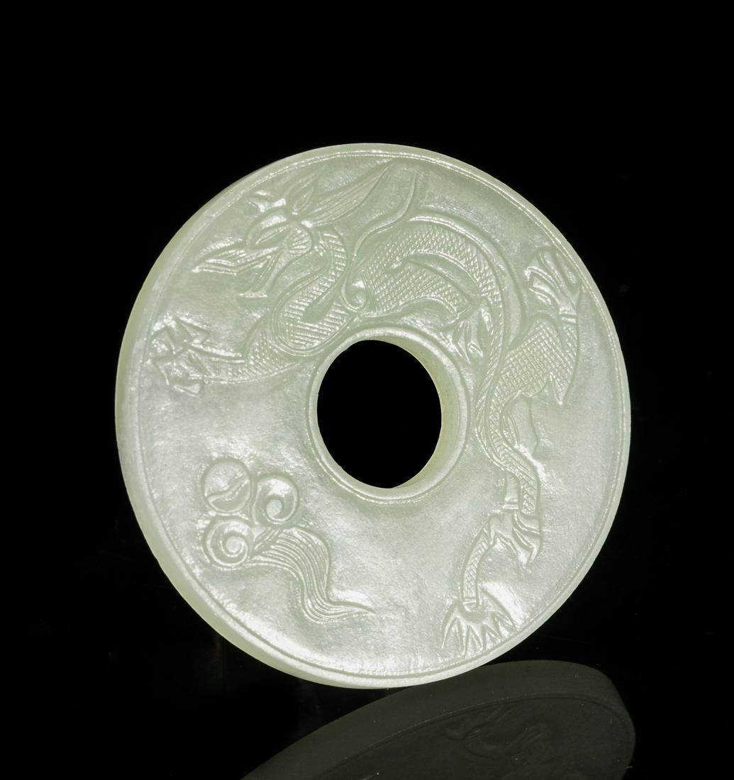 Chinese White Jade Bi: Of circular shape, the center pierced with a circular aperture, one side carved with a phoenix and lingzhi and the verso with a dragon and cloud, the stone in an even white tone. 2.03inch D.