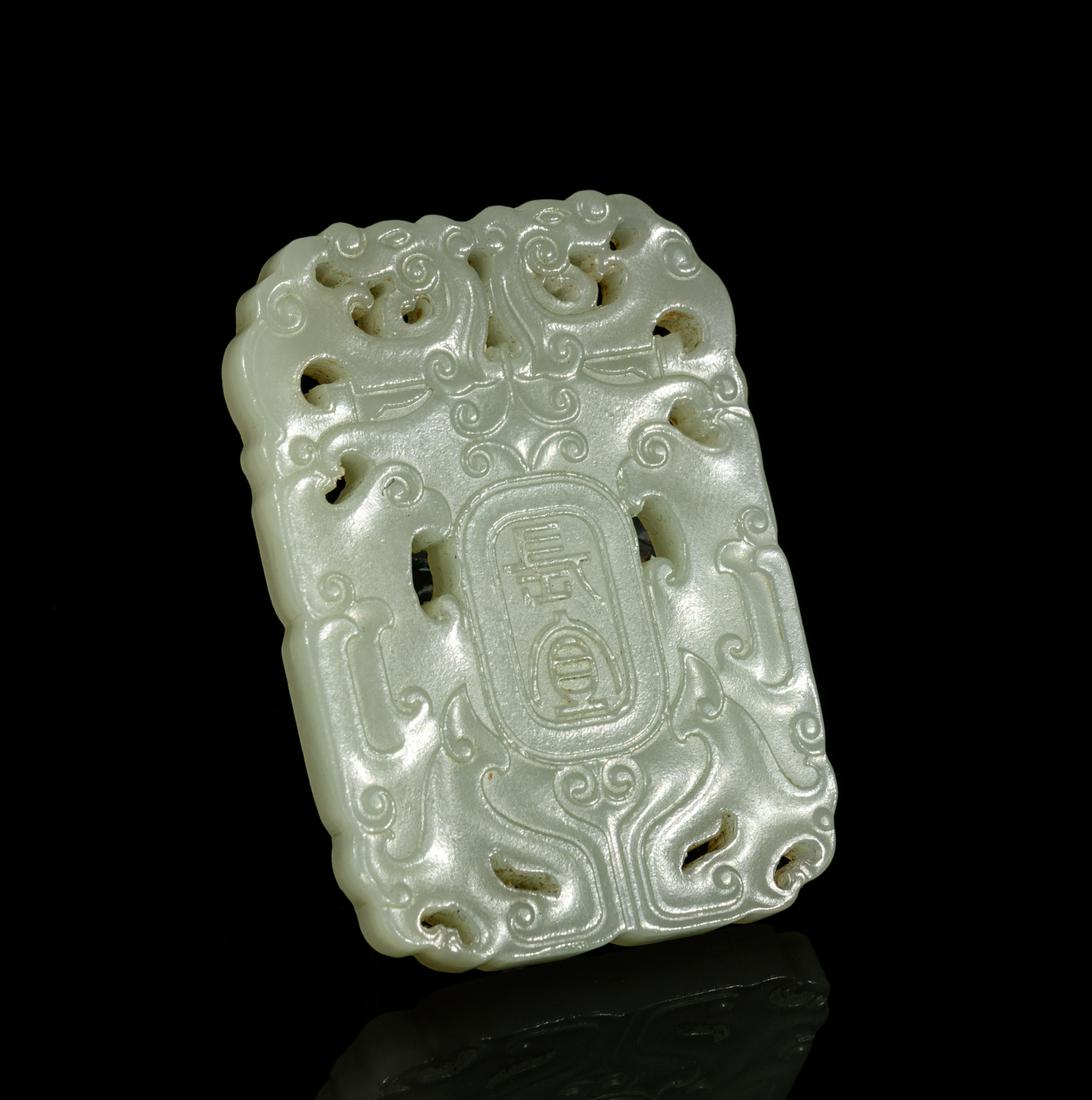 Chinese White Jade Plaque: Of rounded rectangular form, carved in openwork with a pair of stylized archaic birds embracing the central cartouche of two ancient characters, the stone in an even pale celadon tone. 2.5inch L, 1.8i