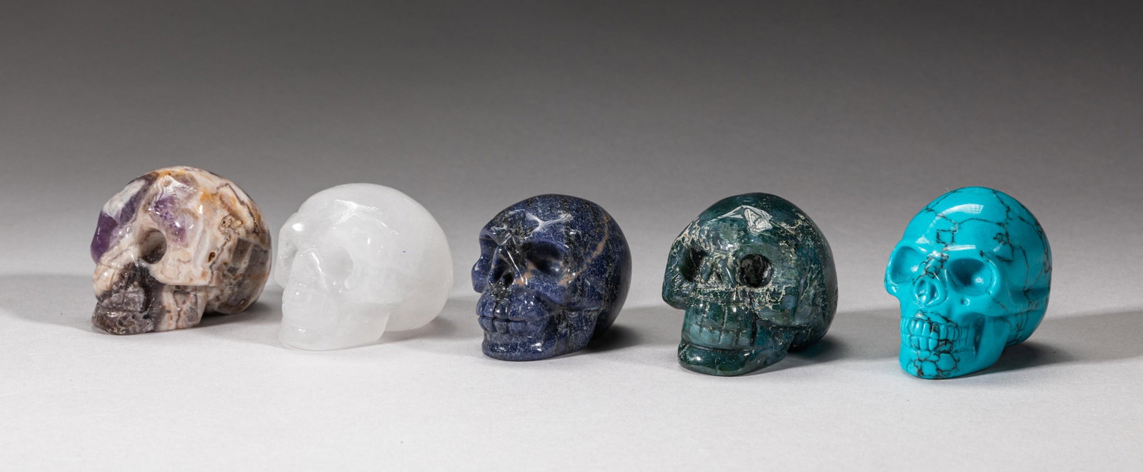 Rare Gemstone Skull Sculptures: Group of five crystal, amethyst, lapis, moss agate and turquoise like carved skull sculptures. 1.95inch L, 1.25inch W, 1.5inch H (largest).