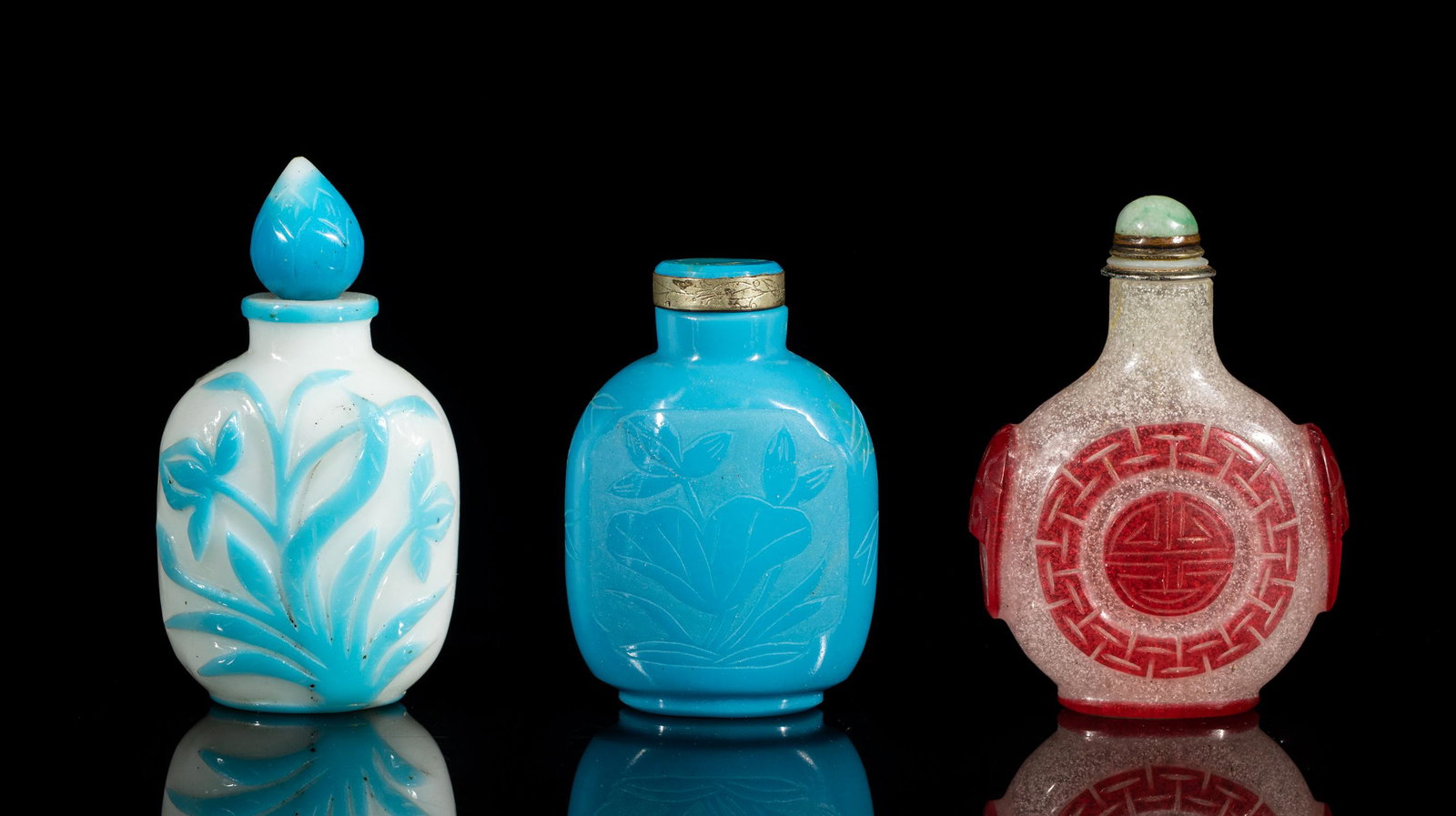 Old Chinese Carved Glass Snuff Bottles: Three as a group: of rounded square form carved with blooming flowers in blue on an opaque white ground, with a lotus bud type stopper; of rounded square form, the opaque blue glass carved in low reli