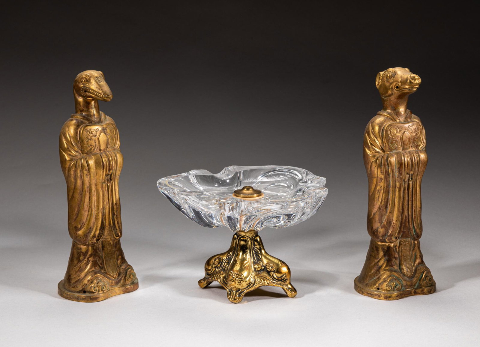 France Louis XvI Type Chinese Figure Sets: Including a triple-petal glass ashtray supported on a metal flower type stand, and a pair of gilt brass figurines with a cow or snake head, dressed in long flowing robes carved with phoenix and dragon