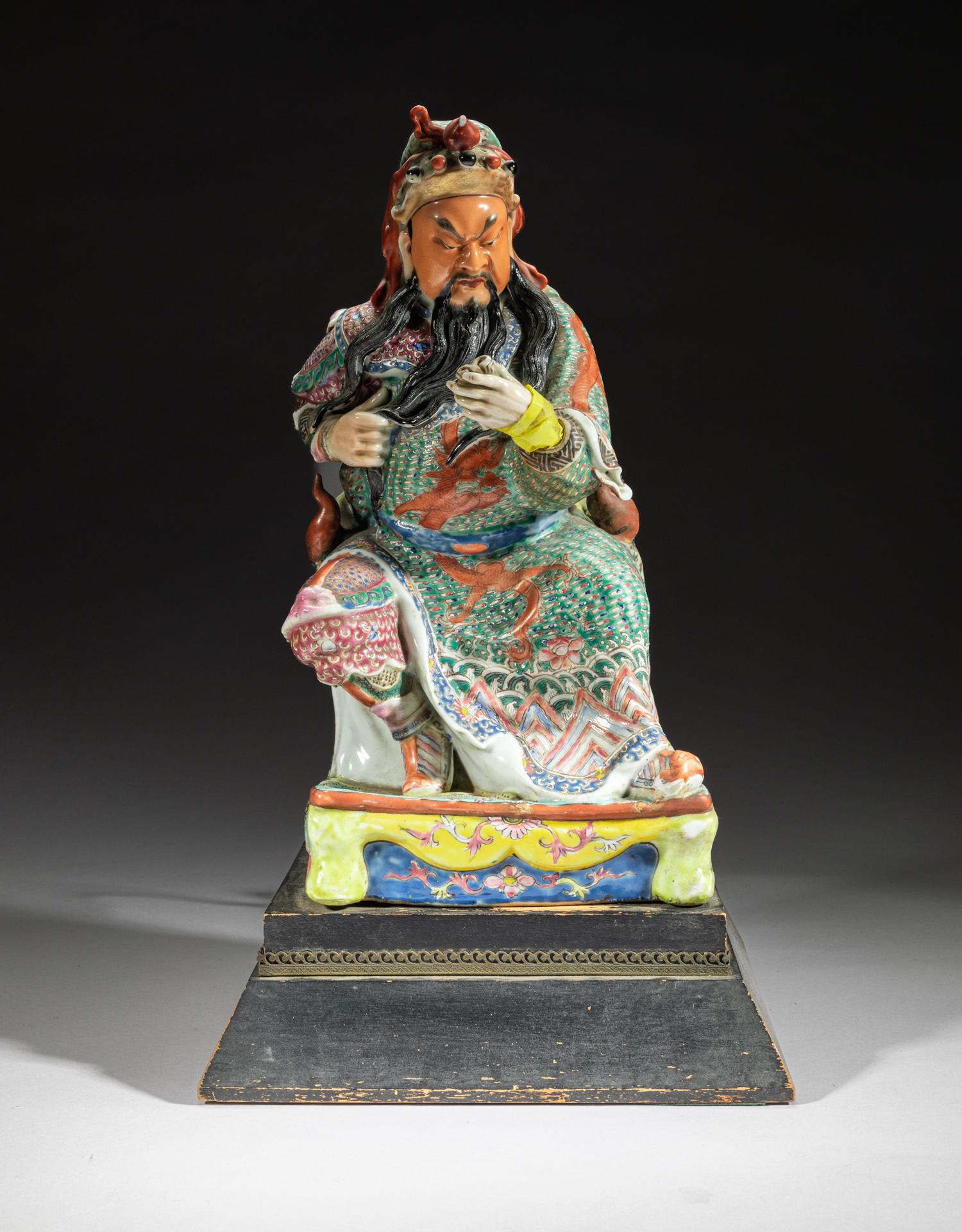 Large Chinese Famille Rose Porcelain Figure: Modeled as a seated ancient general with left hand holding a book and right hand stroking beard, the robe painted with a sinuous dragon among clouds. 16inch H, 9.5inch L, 8.4inch W.