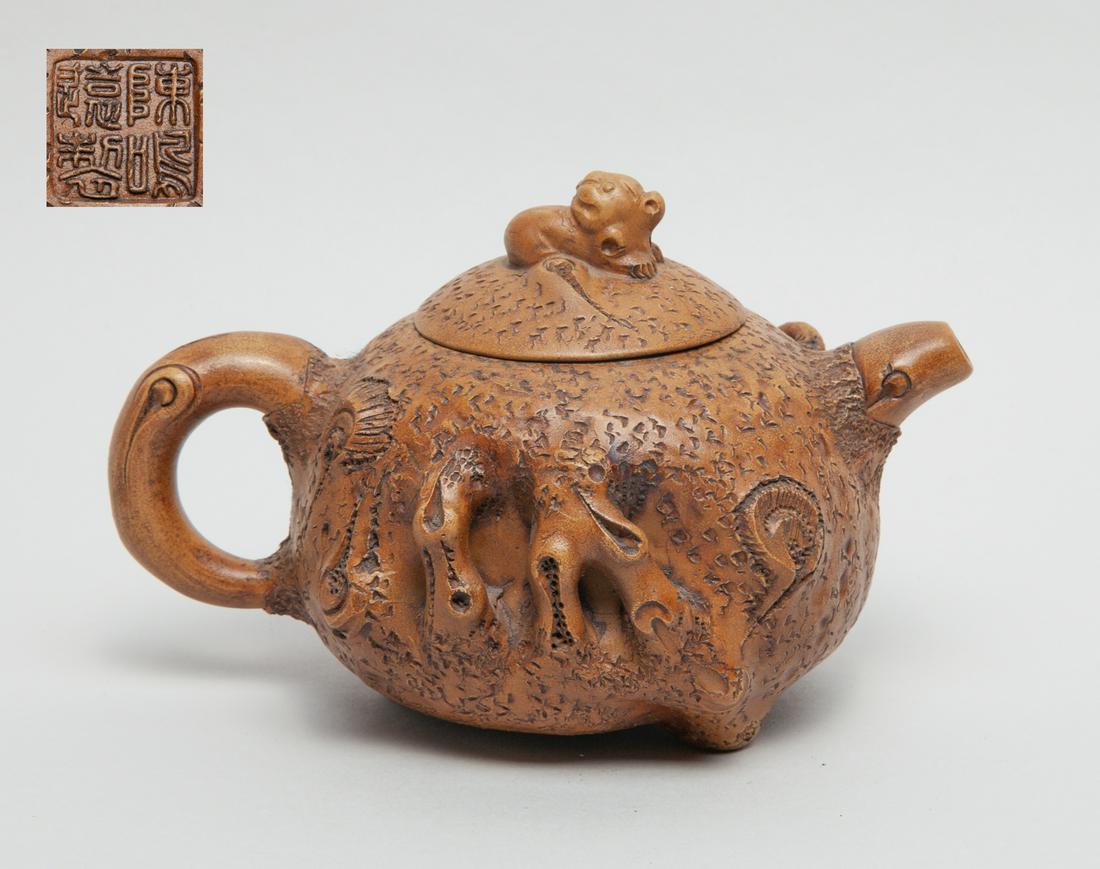 Collectible Chinese Zisha Tea Pot: The pot surface worked in tree trunk form, carved in high relief with leafy and fruiting peach branches, the cover with a beast finial, the cover interior incised with two marks and the bottom with a