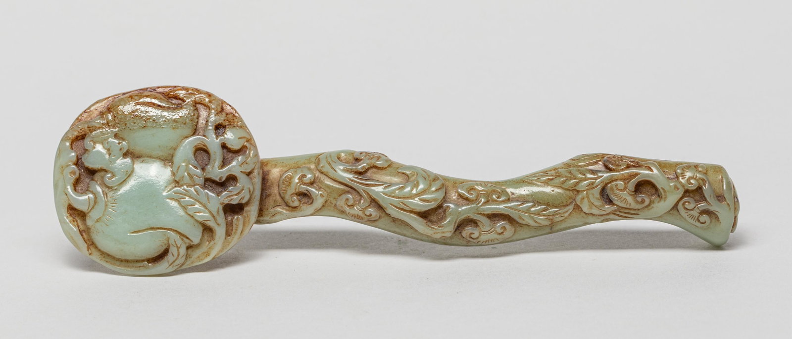Chinese Jade Ruyi Sculpture: The ruyi-shaped terminal carved with two peaches issuing from leafy stem interspersed with a bat, the shaft models in the form of a gnarled stem encircled by leafy branches and lingzhi heads, the cela