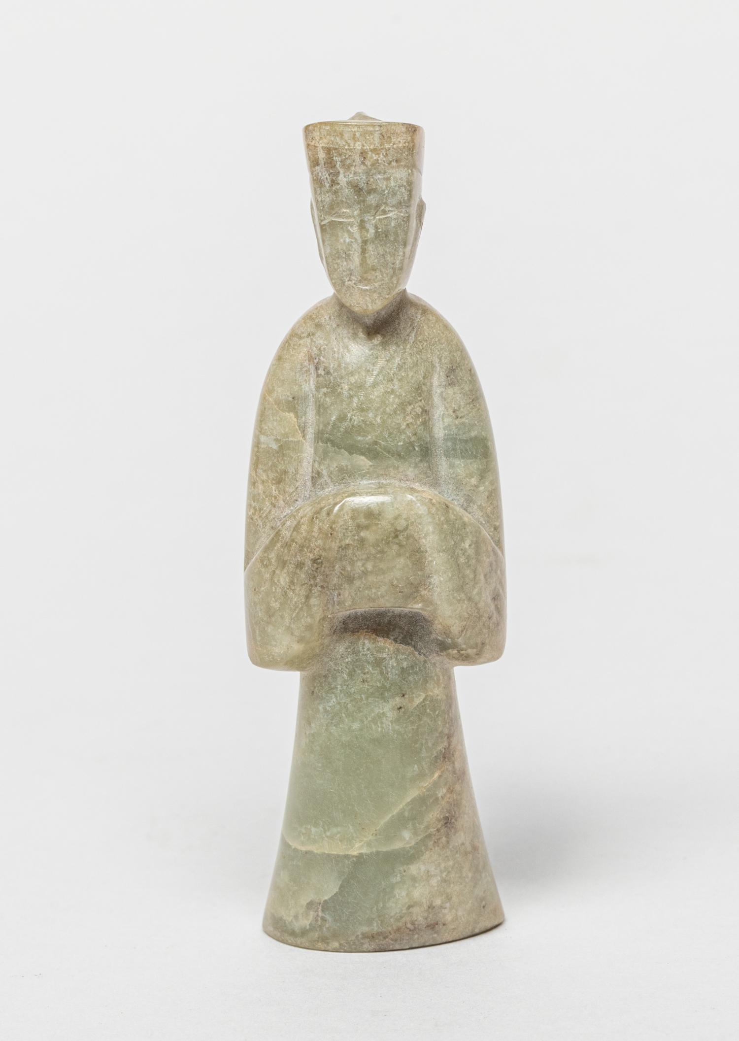 Chinese Jade Carved Figure: Carved in standing figure form, dressed in long loose robe, the stone in mottled grayish celadon color. 3.15inch L, 1inch W. The Estate of T.F. Hookman, German. 1999.