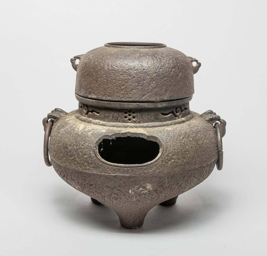 Large Antique Japanese Iron Fireplace: The lower bulb of compressed form resting on three tapered feet, pierced with two apertures and set with two mask loop handles, the upper pot of compressed globular form set with two small handles. 12
