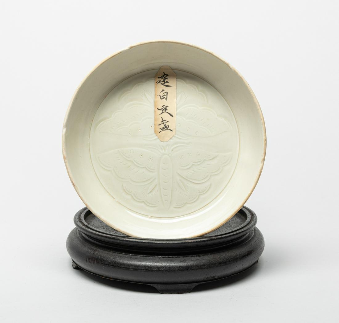 Chinese Ding Stoneware Porcelain Washer: The shallow creamy-glazed washer carved in low relief on the interior with a pair of confronting large butterflies, the unglazed bottom incised with characters, with stand. 6.2inch W. The Estate of Li