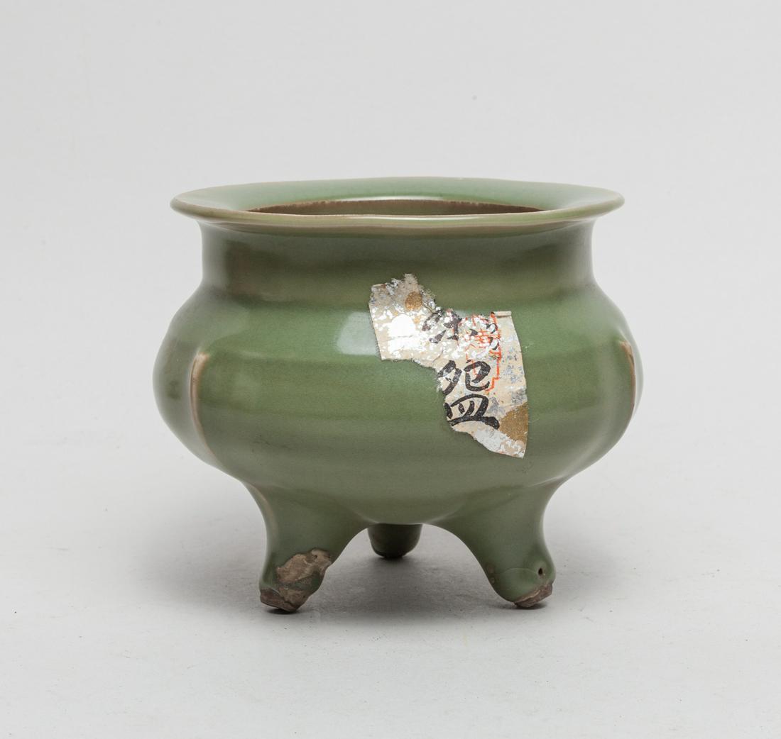 Chinese Longquan Porcelain Censer: The compressed globular body supported on three cabriole legs, rising to a wide cylindrical neck with flat rim, carved with three raised flanges extending from the legs, covered overall with an olive 
