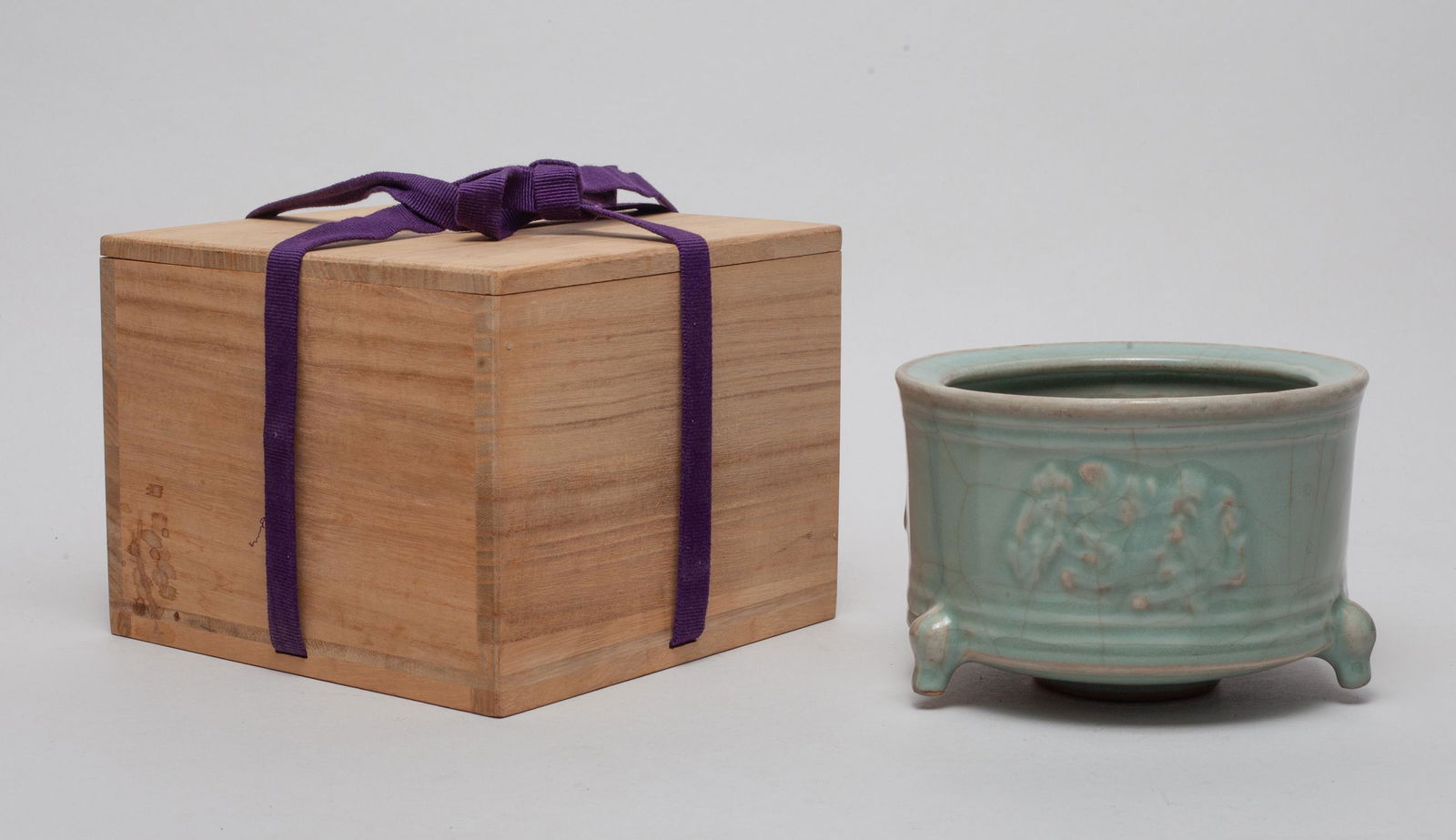 Chinese Longquan Porcelain Censer: Of cylindrical form resting on three short legs, the exterior carved with blooming flowers, covered overall save for the bottom with celadon glaze suffused with brown crackles, with box. Approx. 5.3-3