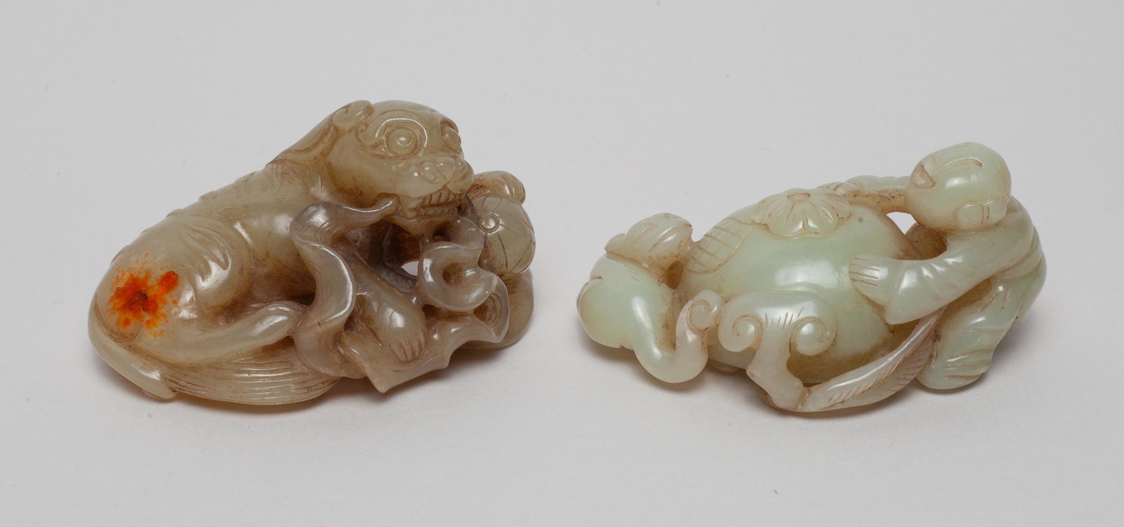 Two Chinese Jade Carvings: One carved as a boy and a dog around a pomegranate fruit issuing from a gnarled stem with lingzhi, the other as a recumbent beast clutching a beribboned ball. Approx. 2.7-1.7-1.1 inch (larger).