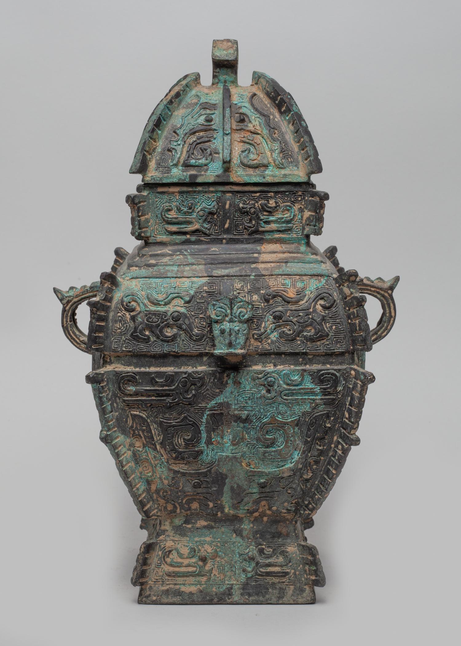 Chinese Cast Bronze Vase: Of square section, flanked by two loop handles, each side cast with taotie masks and archaic beasts on leiwen ground, set with raised flange along the edges, the lid with a capped finial. Approx. 11.7