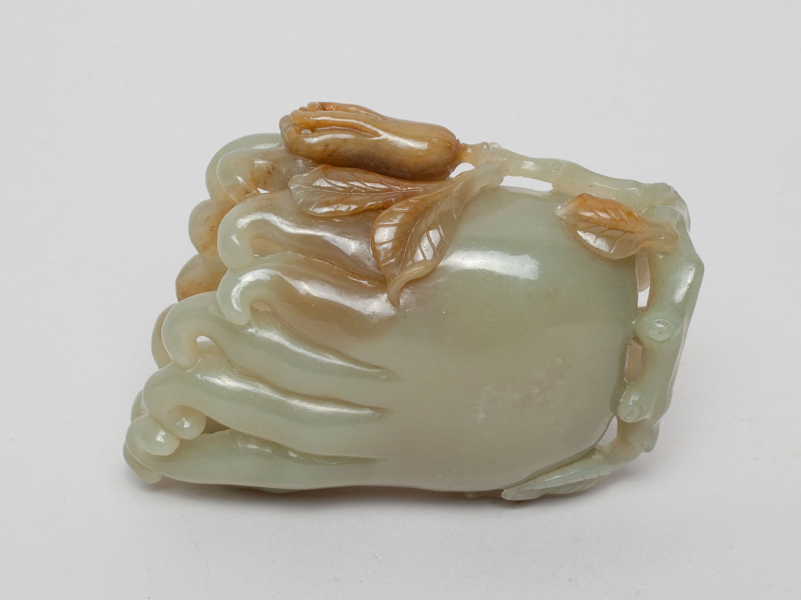 Chinese Jade Carved Sculpture of Buddha Hand: Naturalistically carved as buddha hand fruit issuing from a leafy gnarled stem with a smaller buddha hand fruit, the stone in celadon tone with russet inclusions. Approx. 3.-2.5-1.3 inch.