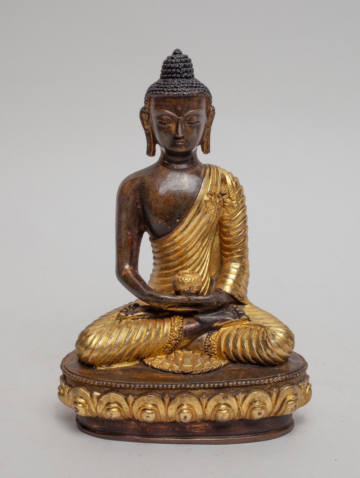Chinese Gilt Bronze Buddha: The Buddha cast seated on a lotus base, the hands holding an elm bowl, the face with serene expression, the bottom with a Buddhist mark. Approx. 7.5-5-3 inch.