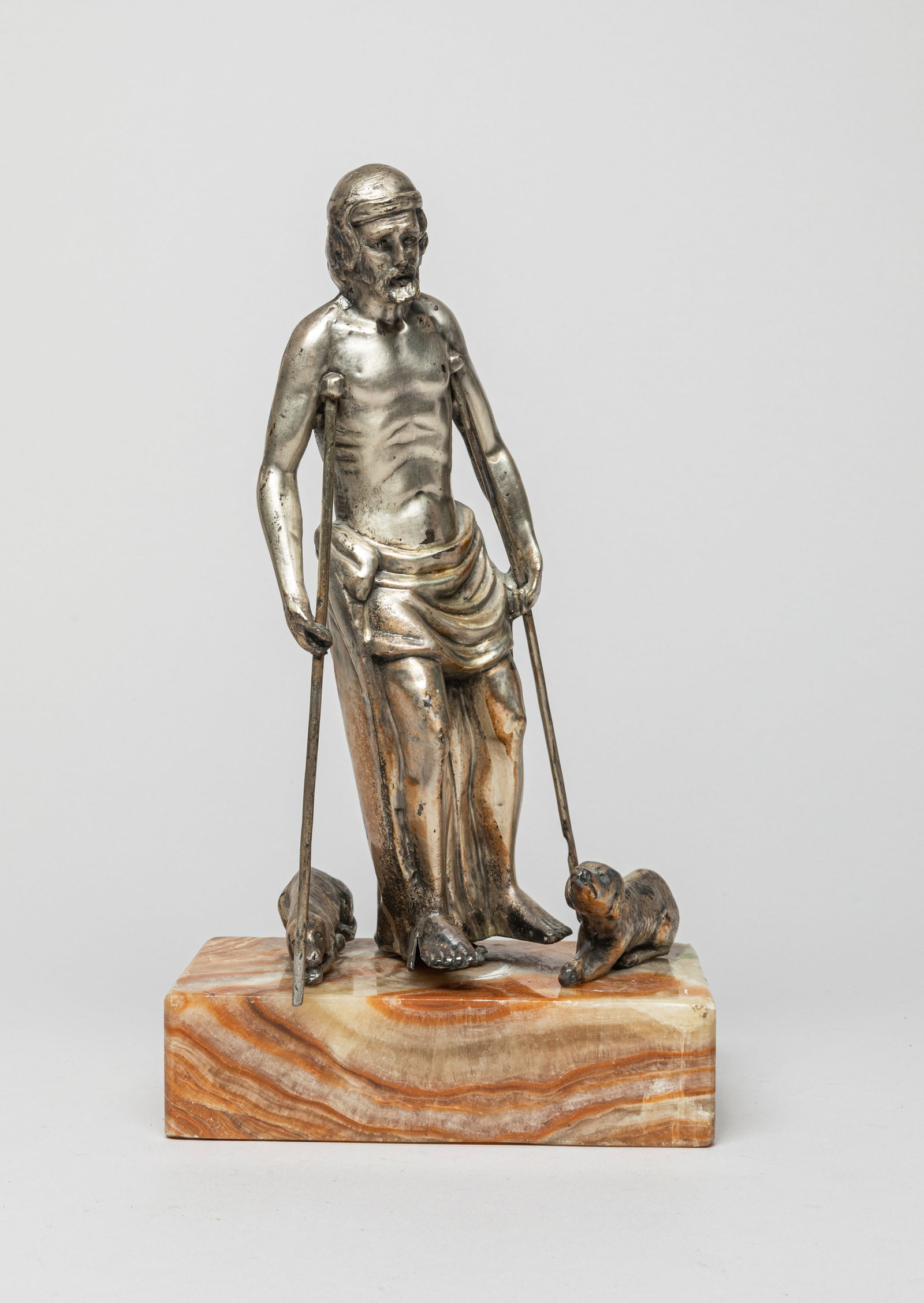 Silver Plated Figure on Marble Stand: The silver-plated figure in a walking pose with a pair of crutches, with two dogs beside. Approx. 6.0-3.2-10.7 inches.