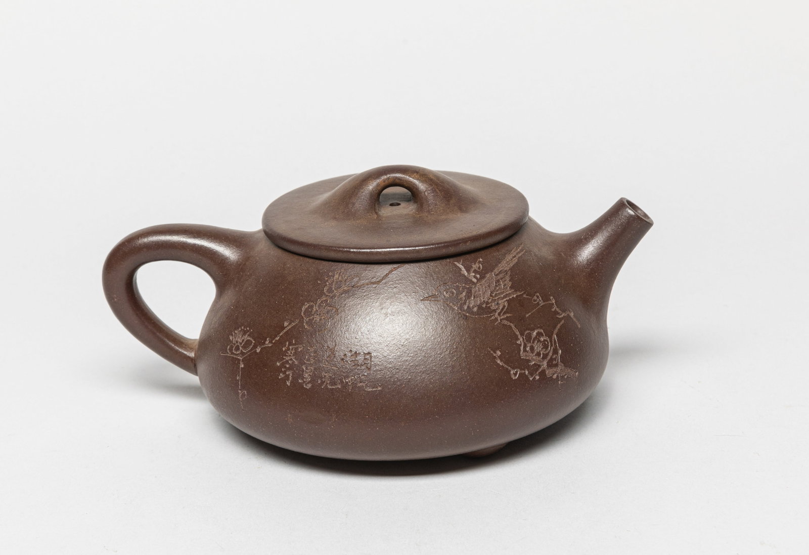 Chinese Yixing Zisha Tea Pot: The teapot body carved with a bird sitting on a plum blossom branch and a Chinese poem on the opposing side, and the bottom carved with characters. Approx. 6.5-4.7-3.0 inches.
