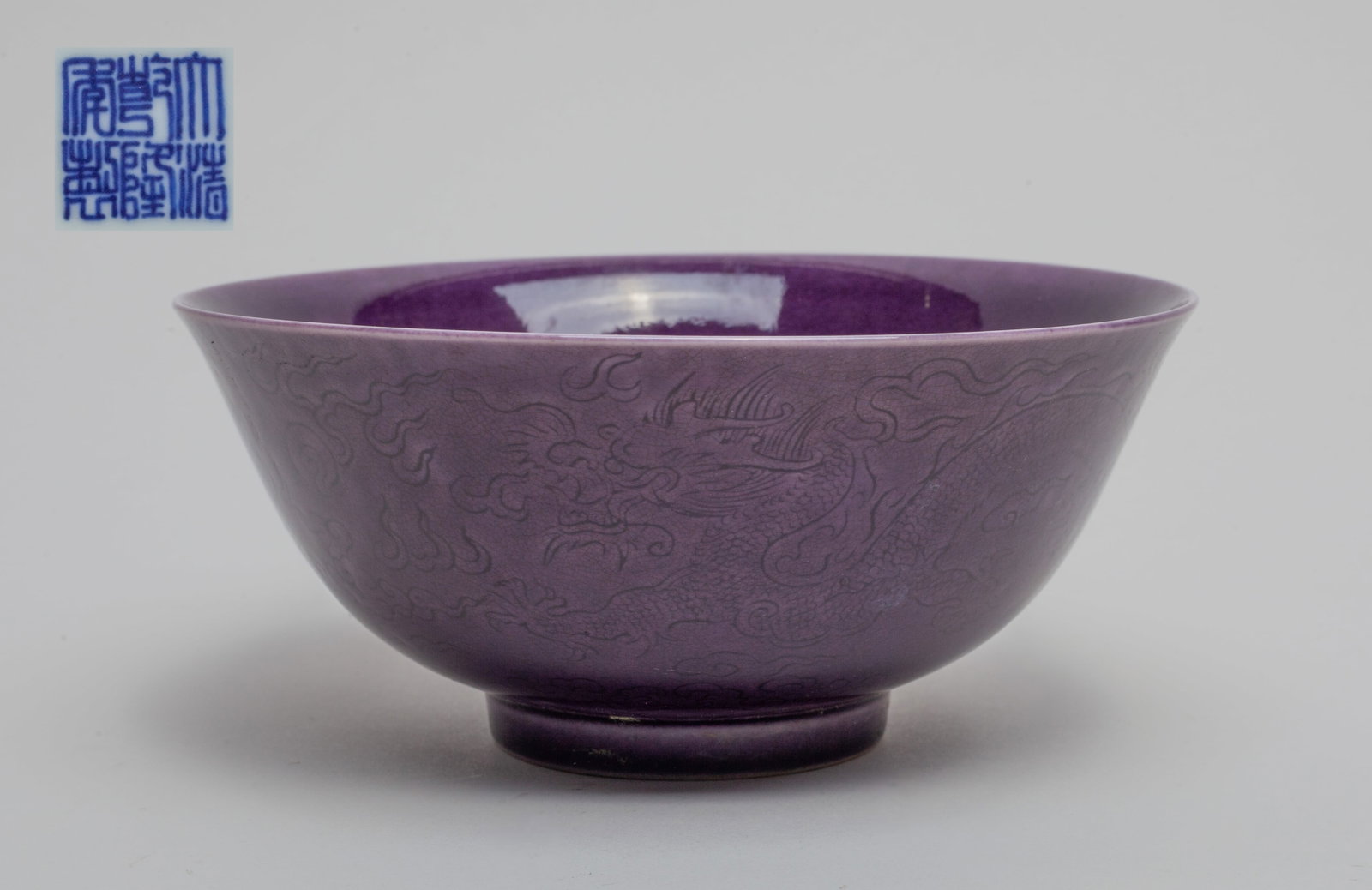 Collectible Chinese Export Porcelain Bowl: Covered in dark purple color glaze, the exterior carved with two dragons chasing each other above a wave motif. The bottom with a mark. Approx. 5.7-2.5 inches.