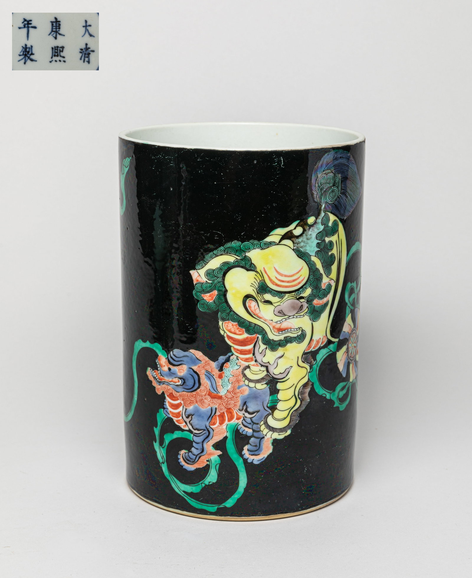 Chinese Wuchai Porcelain Brush Pot: The brush pot of cylindrical form, the exterior applied overall in a black glaze, featuring with two foo dogs, the base inscribed with a six-character mark enclosed in double circles. Approx. 8.1-5.4 