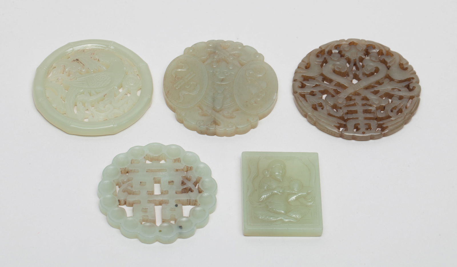 Estate Chinese Jade Pendants: Five pendants as a group: one carved with bird and flowers; one with figure; one with double-happiness symbol; one with foliage and ruyi; and the other with traditional symbols. Approx. 2.3inch D (lar