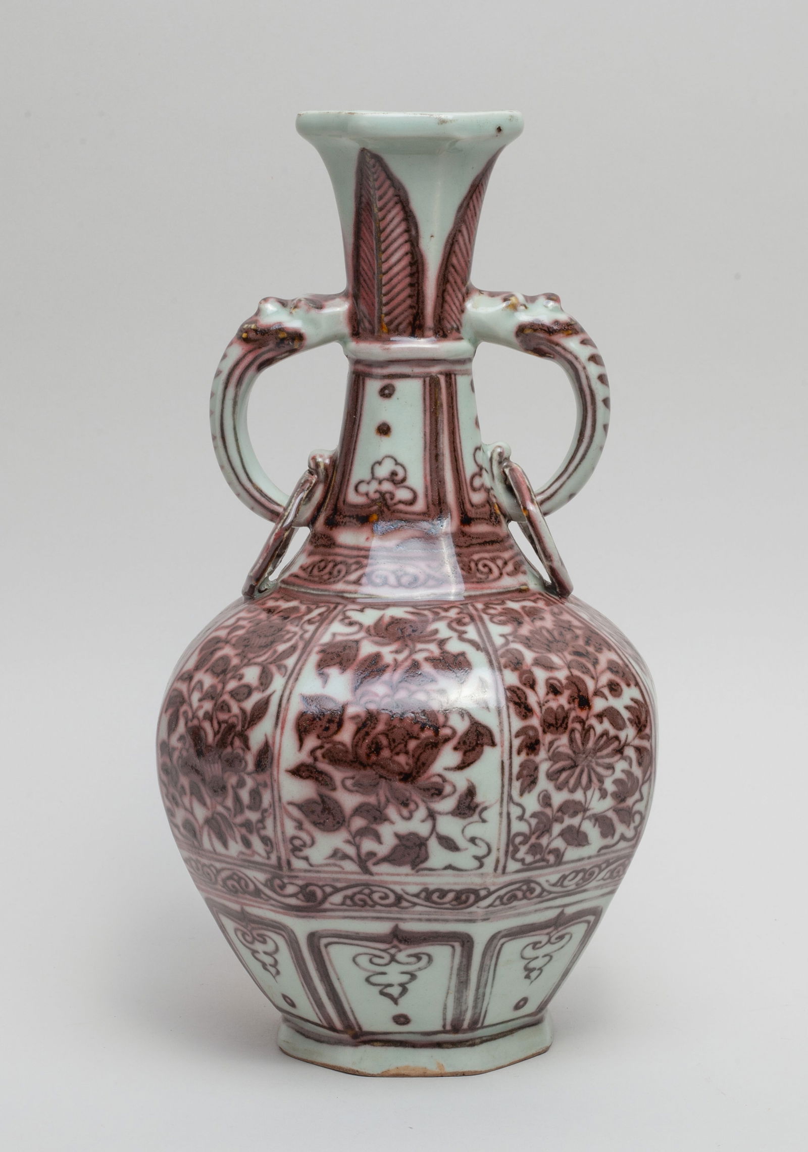 Chinese Copper Red Porcelain Vase: The ovoid body of octagonal section painted with blossoming flowers on each side, above a band of lappets on the foot, the waisted neck flanked by a pair of faux-ring handles, painted with bands of la