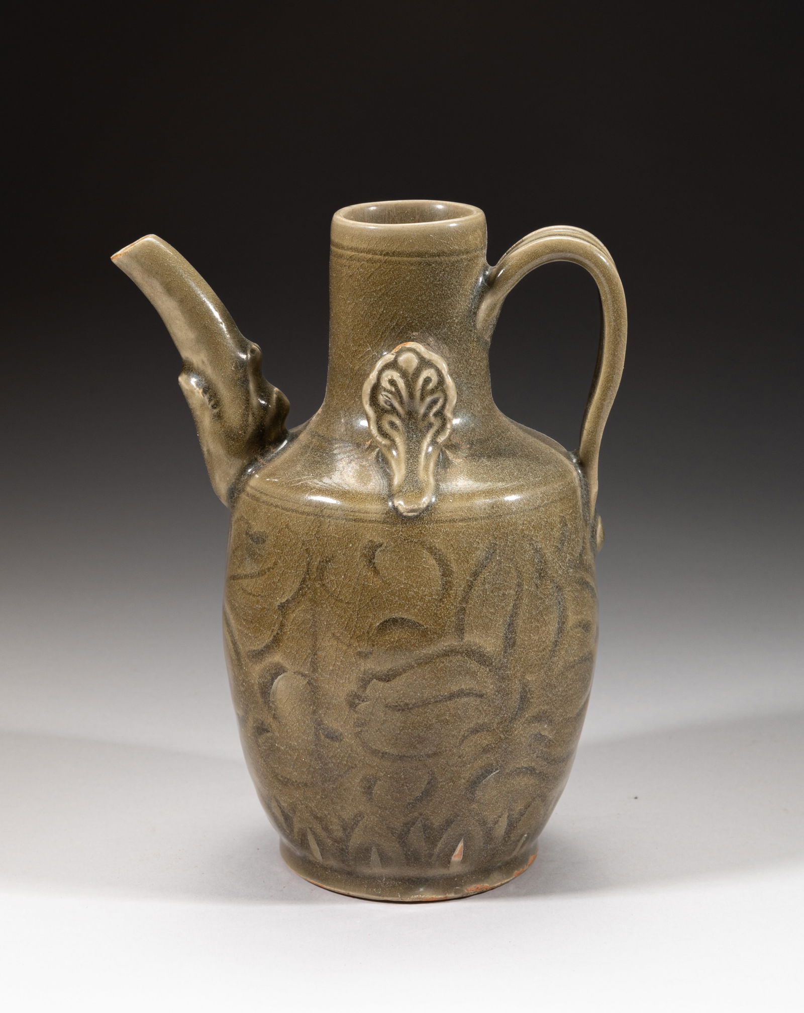 Chinese Shipwreck Yaochou Porcelain Pot: The ovoid body carved in low relief with large lotus blooms above a band of petals, set with two stylized flowers on the shoulder, the spout issuing from a beast head, covered in crackled olive-green