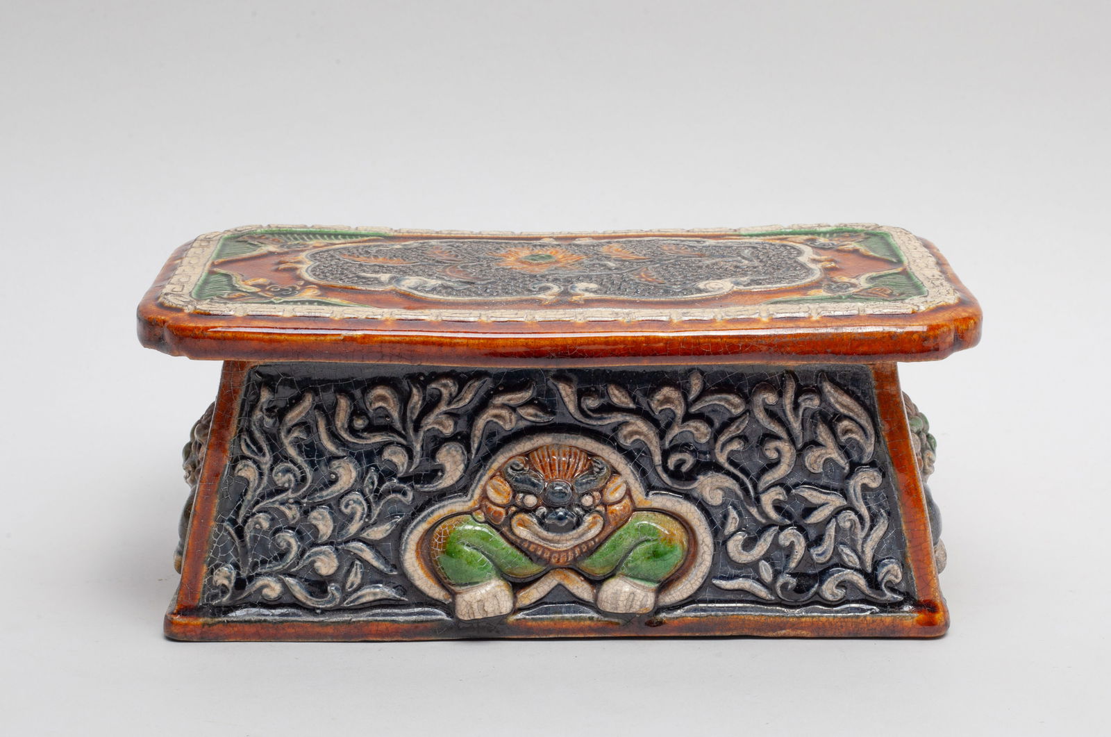 Chinese Sanchai Porcelain Pillow: The pillow top carved with a flower panel at the center, surrounded with bats at the corners, the sides carved with beast amidst foliate sprays, applied in green, brown, beige and dark blue glaze suff