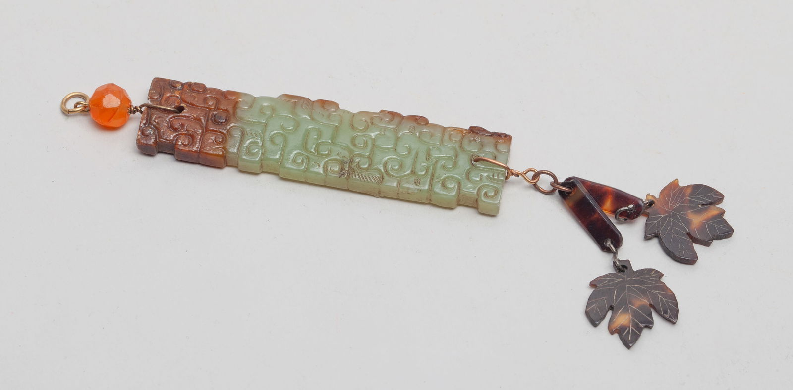 Chinese Russet Jade Pendant: Elongated pale celadon and russet jade pendant, carved on one side with archaistic scrolls, with bead and leaf form pendants. Approx. 2.8*0.68 inch.