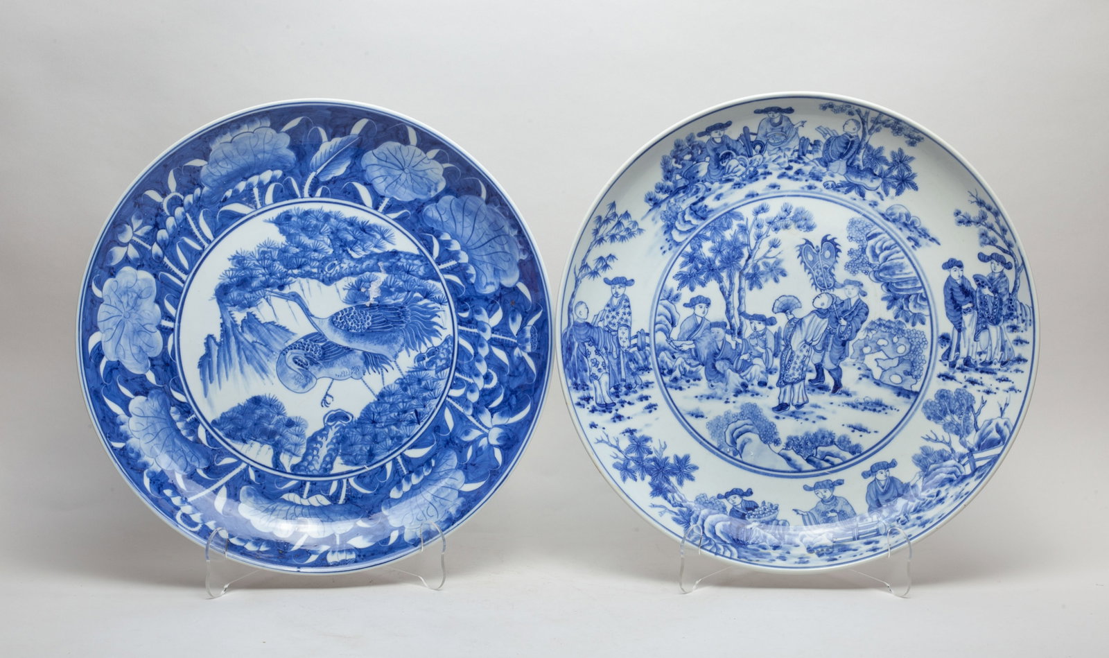 Two Chinese Blue & White Porcelain Chargers: One charger interior painted with figures in various activities in landscape setting, the other charger interior center painted with a pair of cranes and pine trees, framed by a band of lotus. Approx.