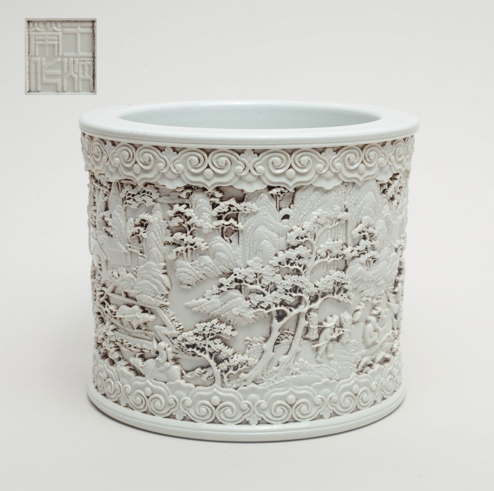 Chinese Blanc De Porcelain Brush Pot: Of cylindrical form, the exterior carved in high relief with a continuous landscape scene, overall covered in white glaze, the bottom carved with a seal mark. Approx. 5.7*4.8 inch.