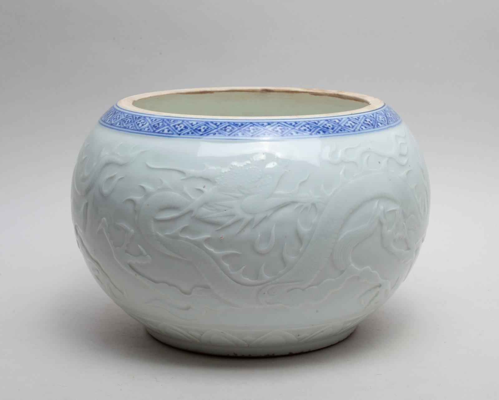 Large Chinese Export Porcelain Washer: Of ovoid form, the exterior carved with sinuous dragons pursuing flaming pearls amidst clouds, above a band of overlapping lotus petals. Approx. 6.6*9.8 inch.