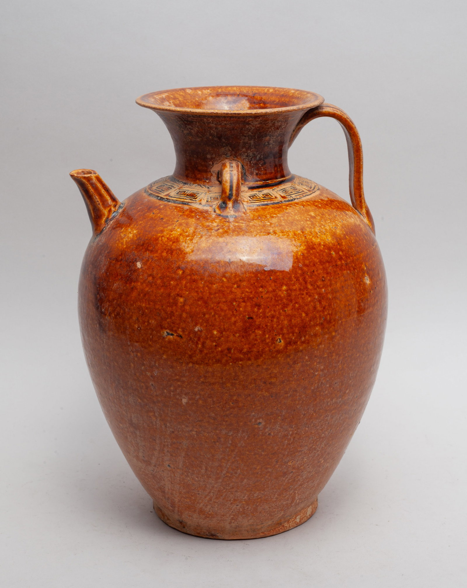 Chinese Sanchai Stoneware Vase: Of ovoid form with a spreading mouth, flanked with a handle and a spout, carved around the neck with a fret band, the exterior and interior applied in mottled caramel-brown glaze. Approx. 11*7.7 inch.