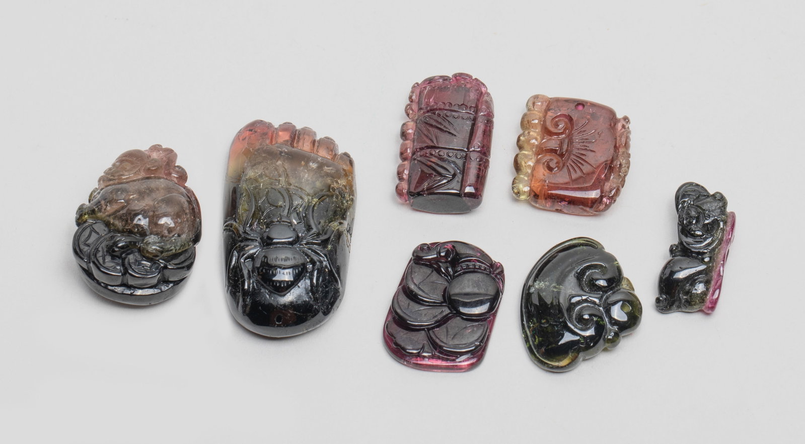 Chinese Wine Red Tourmaline Pendants: Group of seven Chinese wine red tourmaline pendants, carved in form of: bamboo; lingzhi; coins; lingzhi, coin and bat; foot, spider and coins; foo dog and coins; or lingzhi and bat. Approx. 50 gram (t