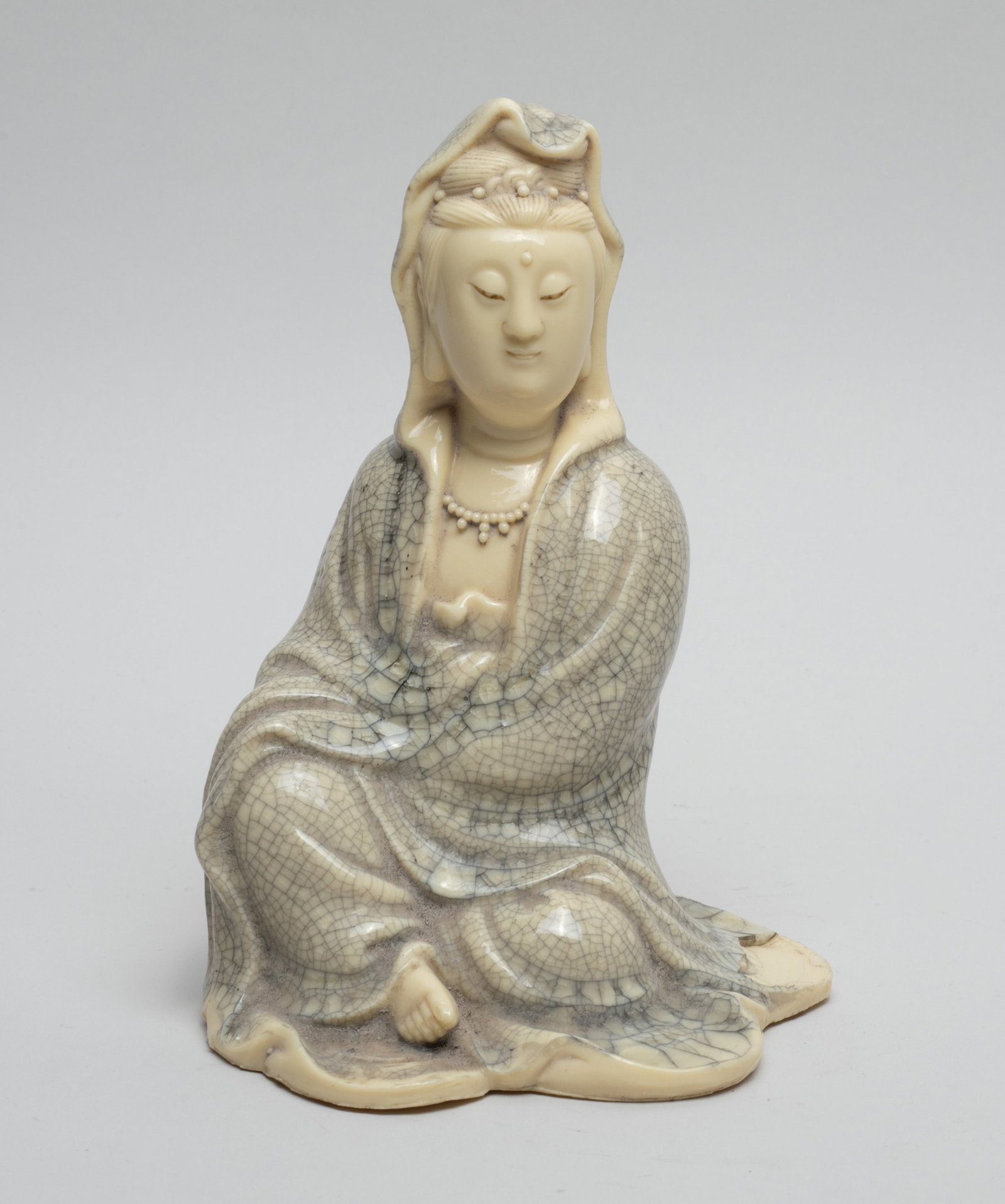 Chinese Porcelain sculpture of Kuanyin: Chinese porcelain seated Kuanyin sculpture, wearing a loose-fitting robe suffused with a matrix of black crackles, the face with serene expression. Approx. 4.7*4.1*6.6 inch.