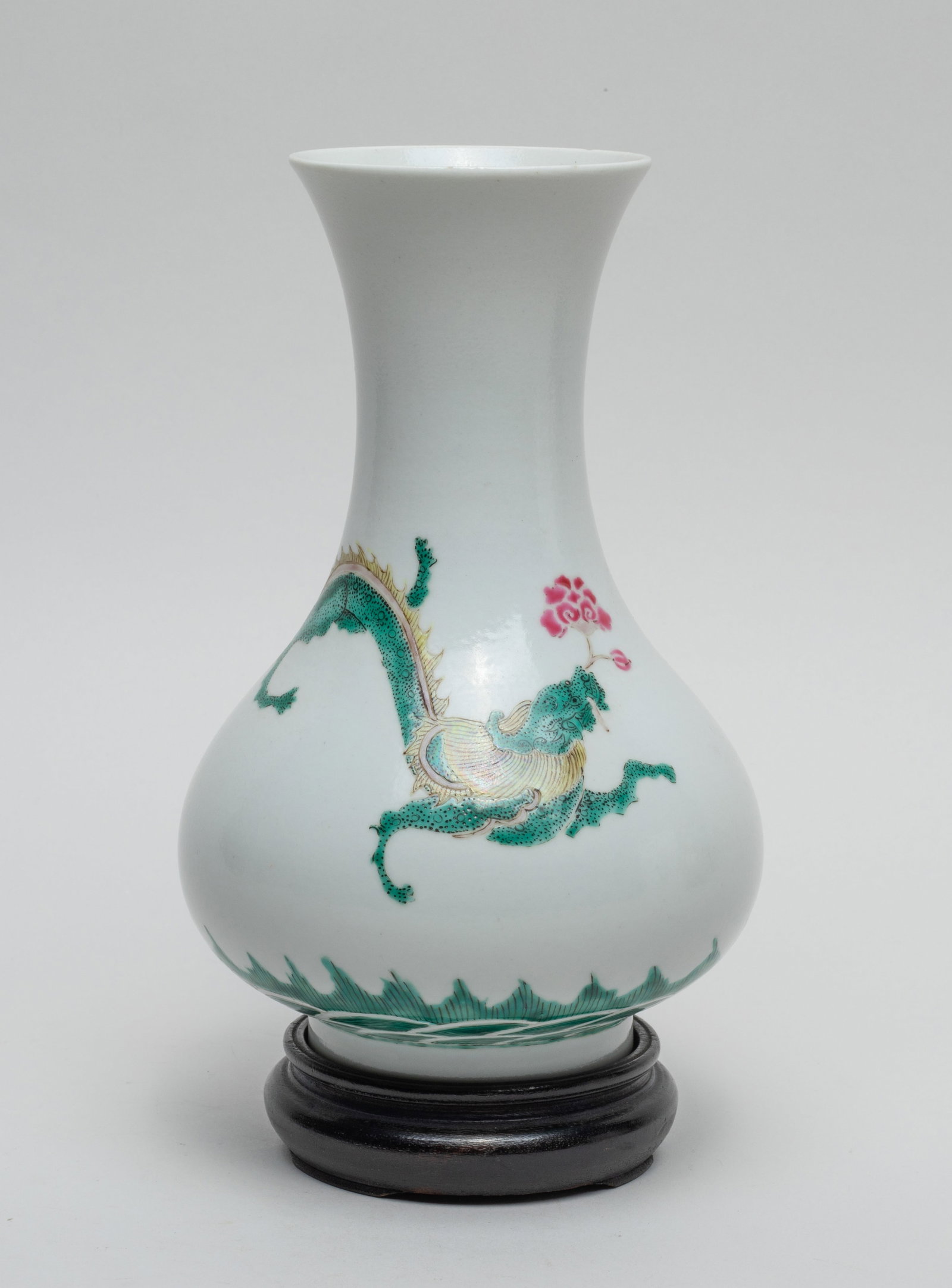 Chinese Famille Rose Porcelain Vase w/ Stand: The pear-shaped body rising from a short foot to a waisted neck and a flared rim, enameled and painted with a dragon sinuous above waves, grasping flower in the mouth, with wood stand. Approx. 7.9*4.5