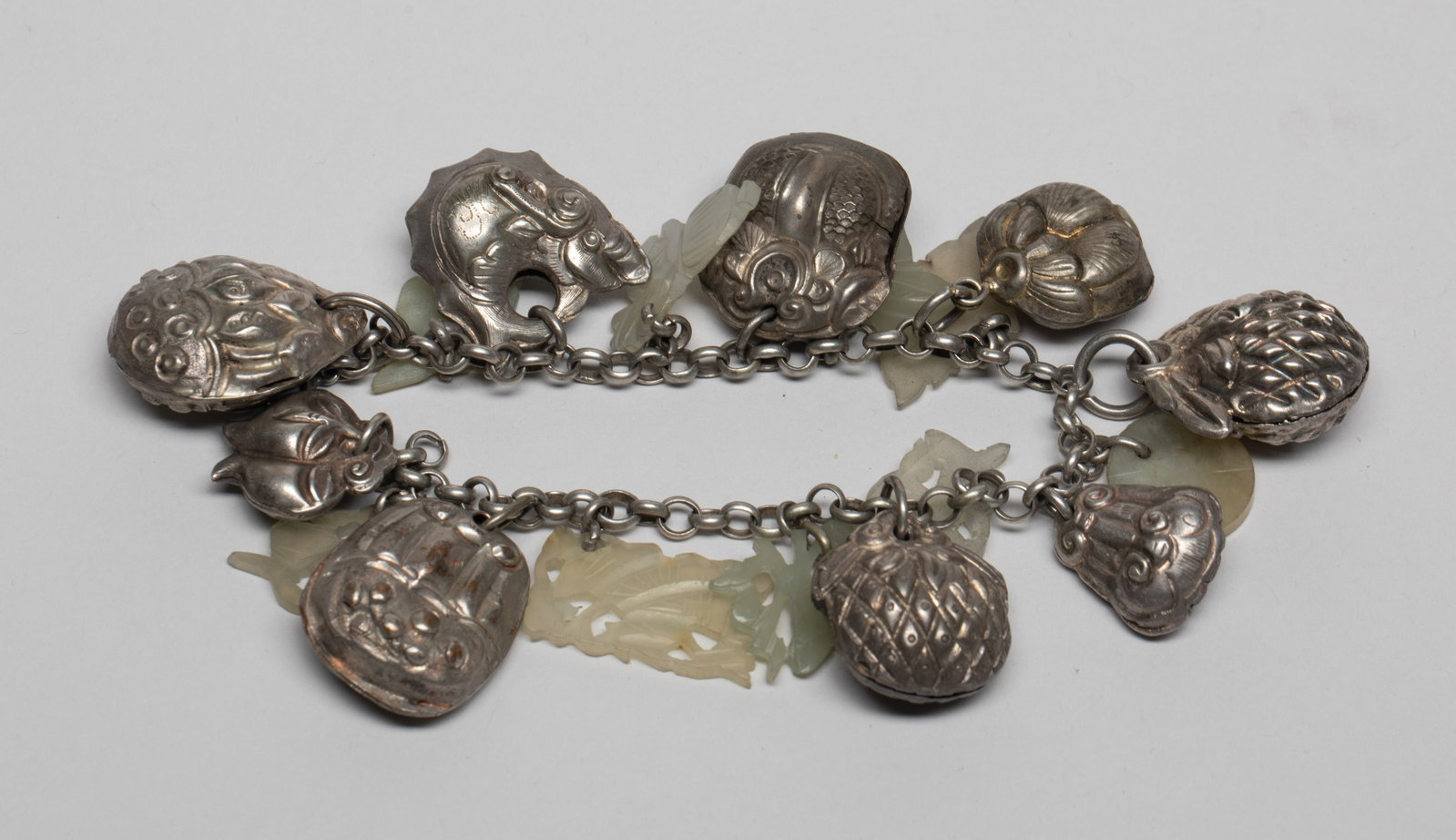 Chinese Jade & Silver Tone Bracelet: Chinese chain bracelet, suspended with jade toggles carved in flower or traditional symbol form, and silver-tone charms worked in fruit, lotus, lingzhi or fish form. Approx. 7inch L.