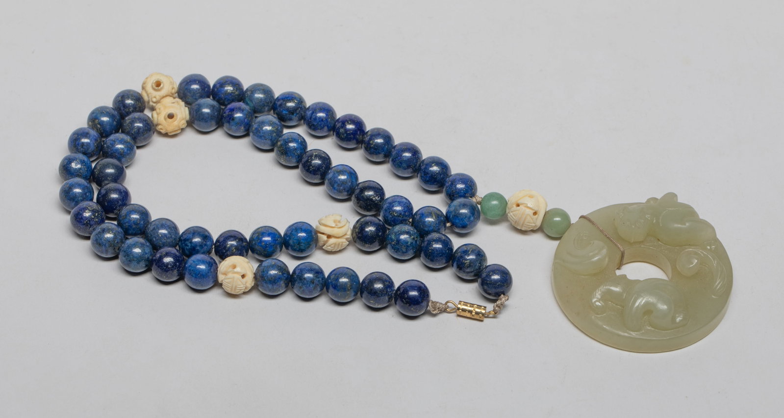 Chinese Jade Pendant w/ Lapis Necklace: Chinese jade pendant of circular shape, one side carved in high relief with a sinuous chilong, the reverse incised with archaic scrolls, suspended on lapis bead and bone bead necklace. Approx. 22inch 