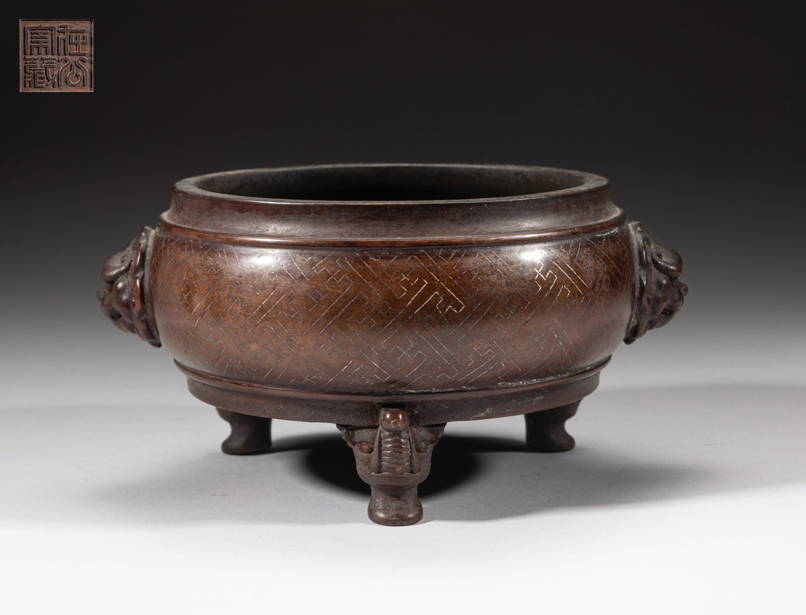 Chinese Bronze Cabinet Censer: The compressed body decorated with a fret band, set with a pair of raised beast masks as handles, supported on three beast form legs, the bottom incised with a seal mark. Approx. 7.2*6.1*3.7 inch.